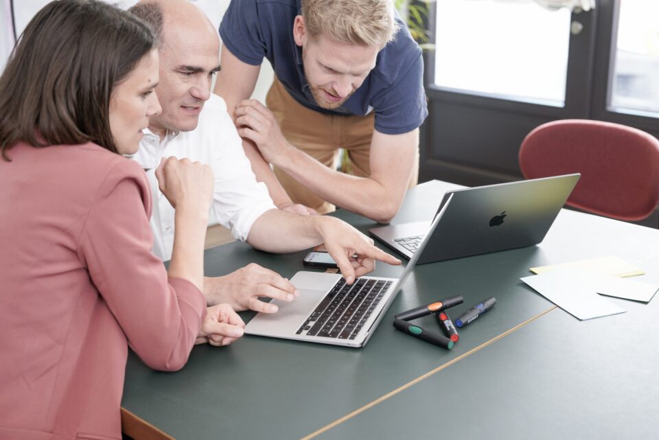 Drei Kollegen arbeiten gemeinsam am Laptop im Büro