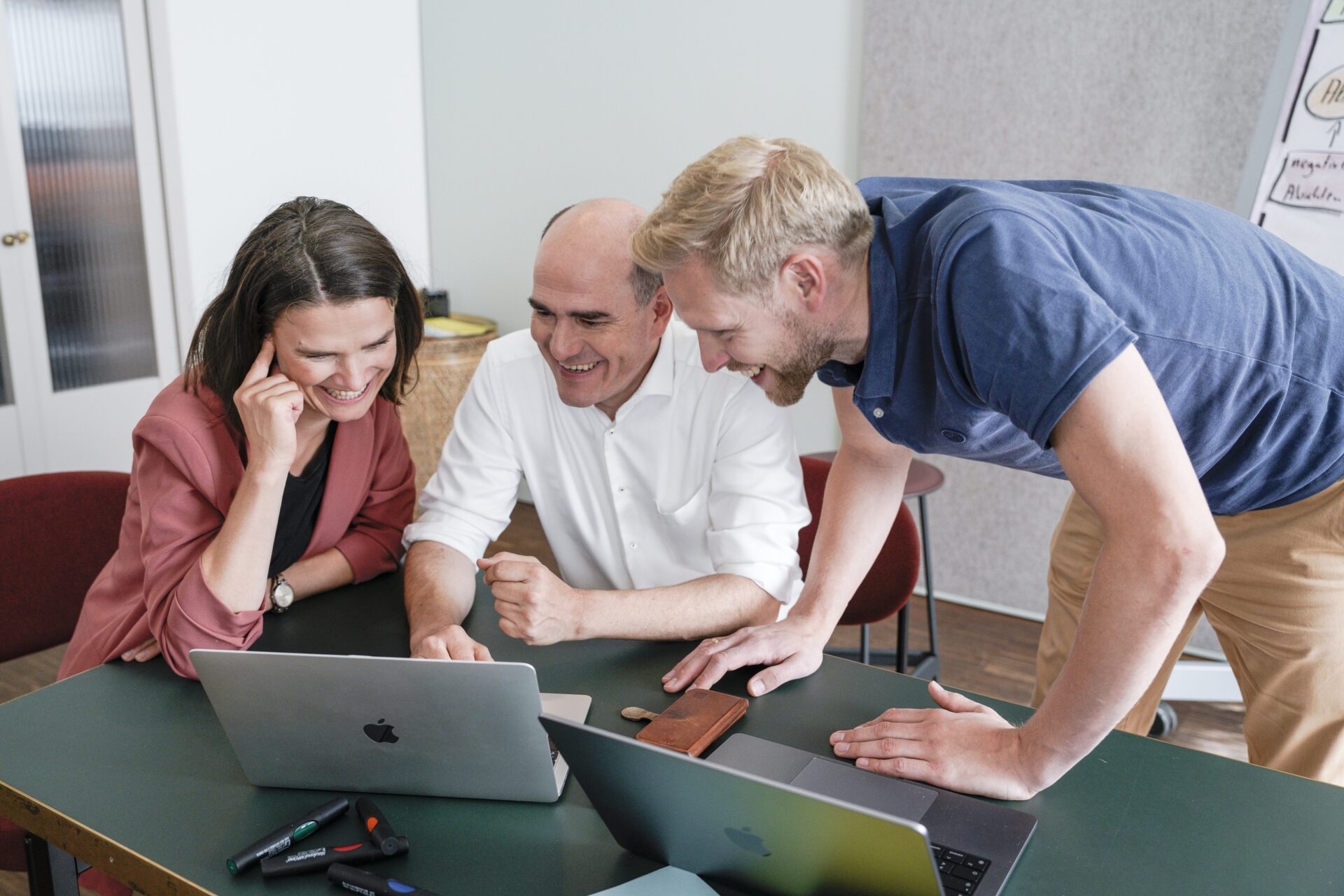 Drei Kollegen lachen gemeinsam am Laptop im Büro