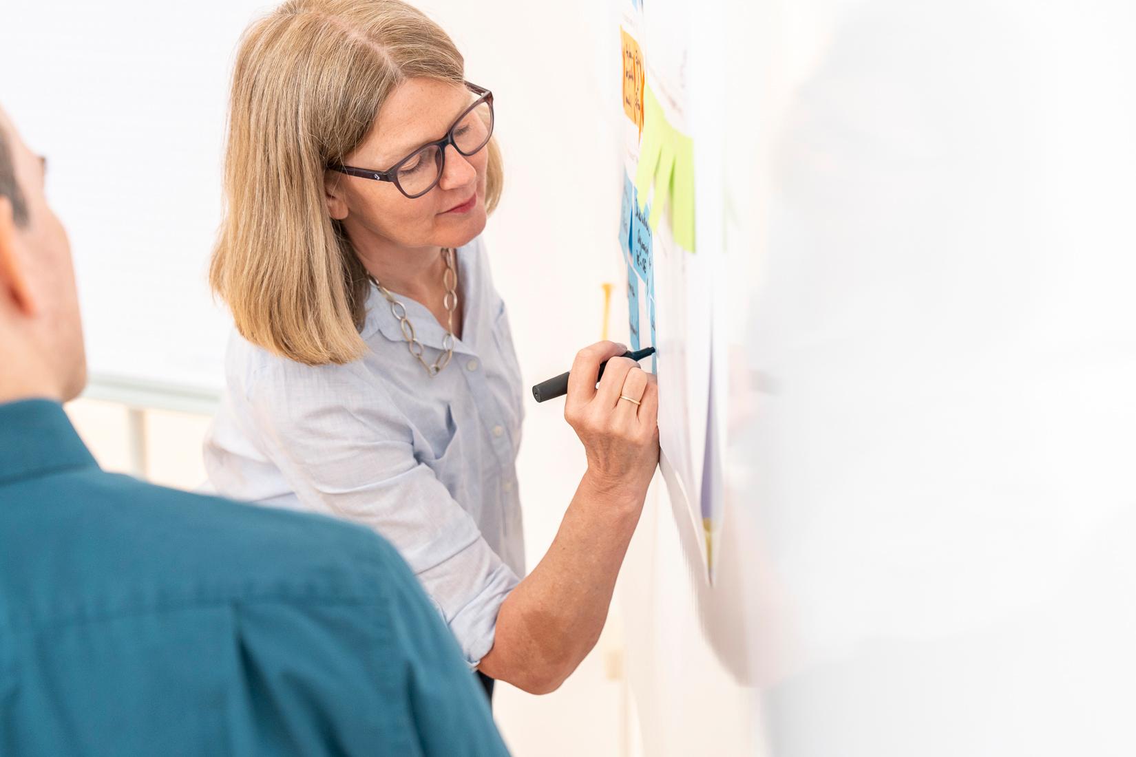 Frau schreibt Notizen auf Haftzettel an Wand