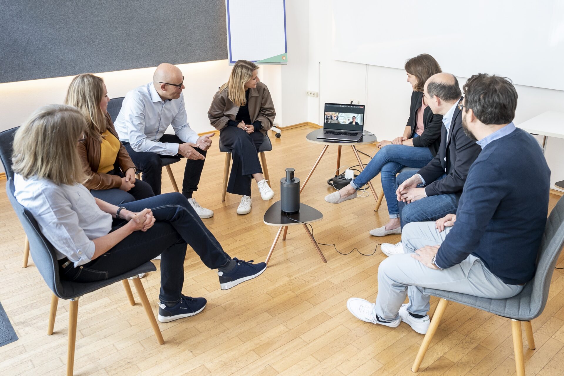 Teammeeting im Kreis mit Videokonferenz am Laptop