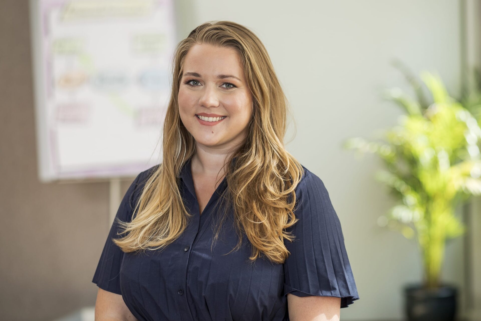 Lächelnde Frau im Büro vor Flipchart und Pflanze