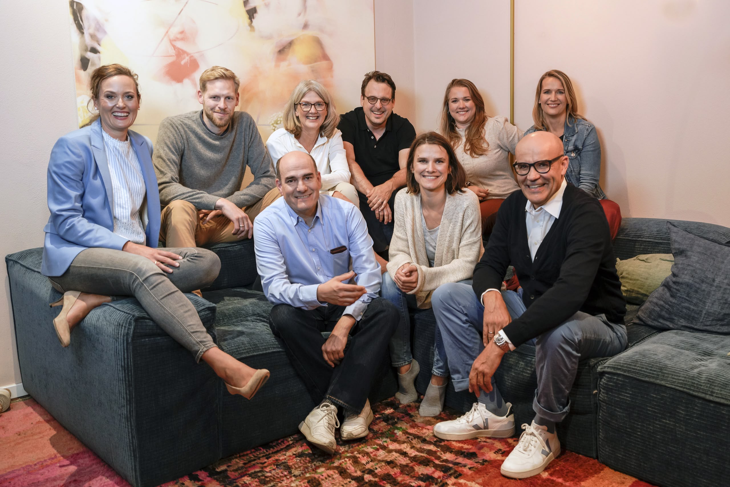 Neun lächelnde Erwachsene auf Sofa im Wohnzimmer