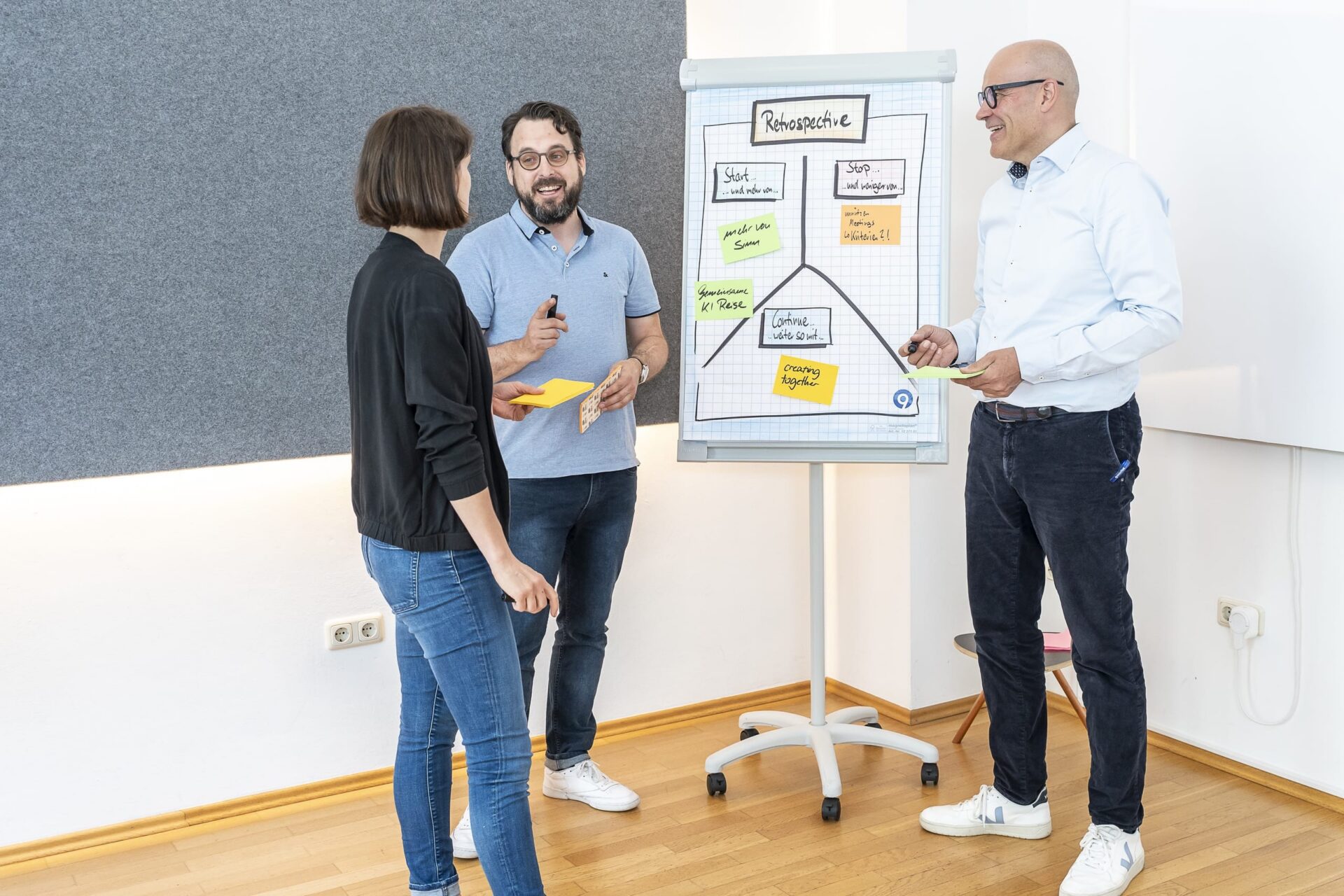 Drei Personen bei Retrospektive am Flipchart im Büro
