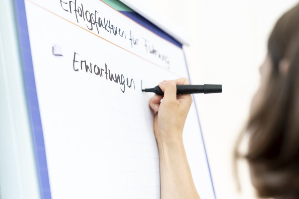 Person schreibt „Erwartungen“ auf Flipchart im Meeting