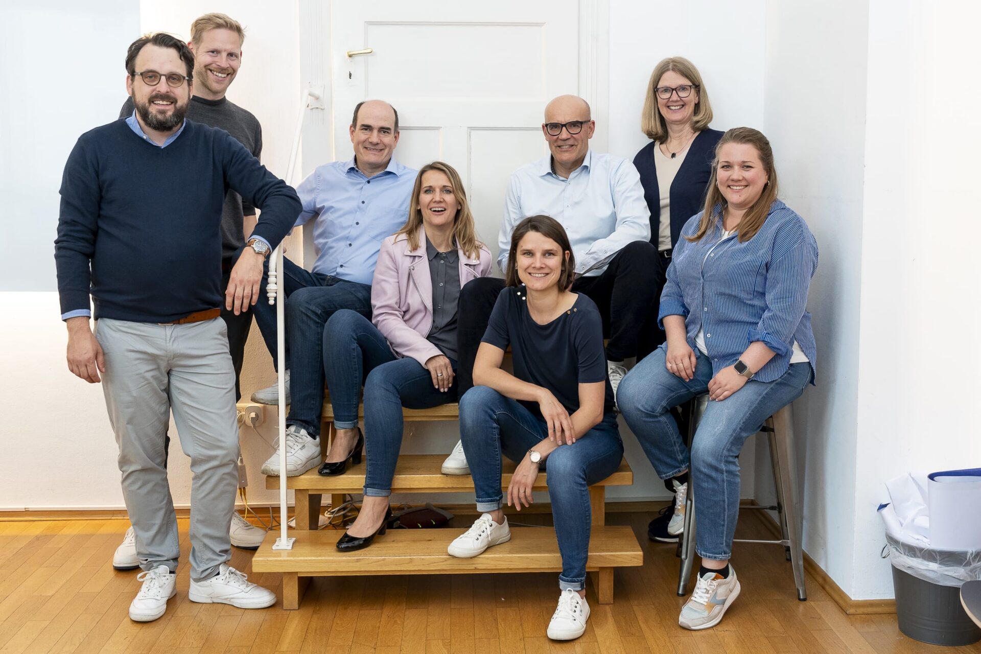 Acht Personen posieren lächelnd auf Treppe im Büro