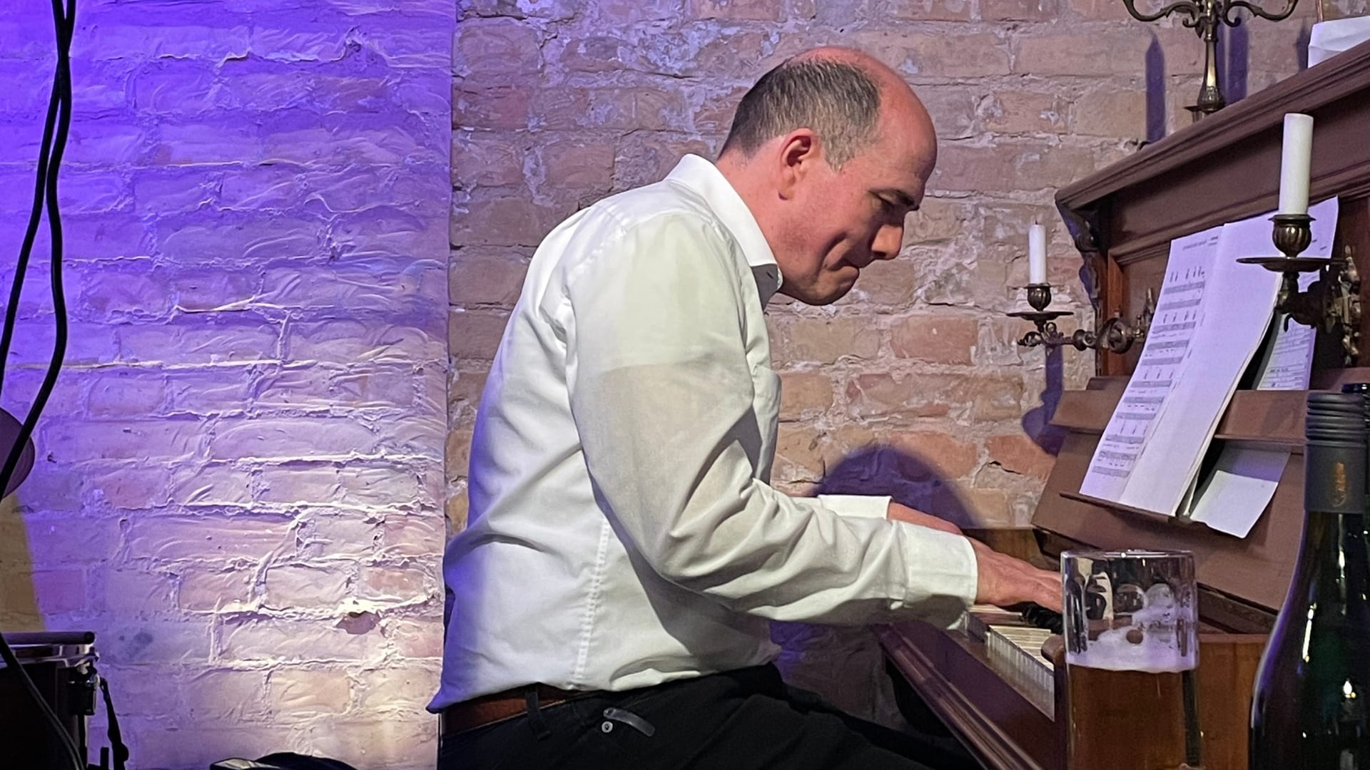 Mann spielt Klavier vor Backsteinwand mit Bierglas