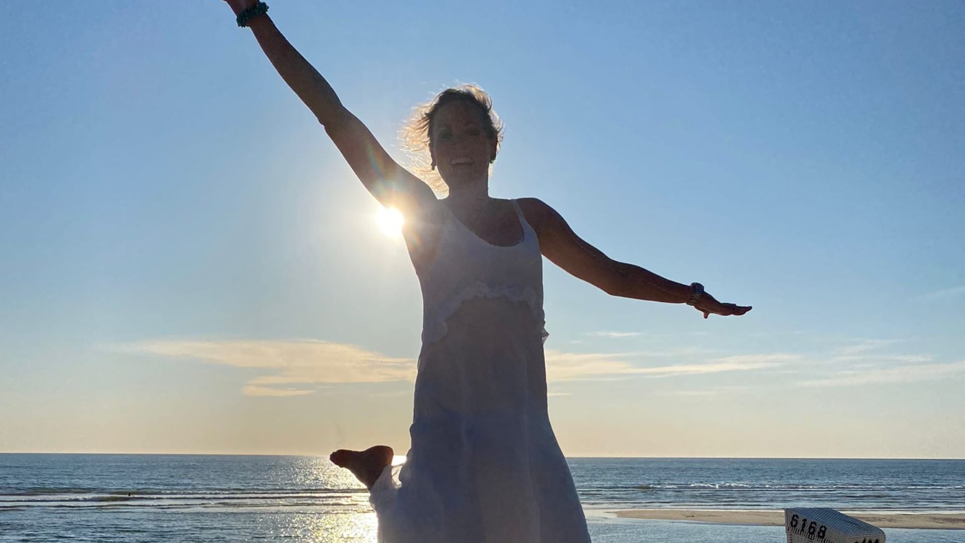 Frau mit ausgebreiteten Armen am Strand bei Sonnenuntergang