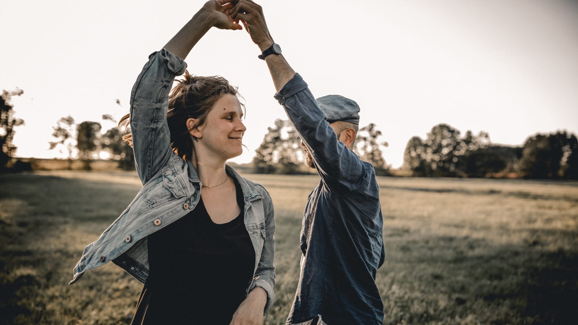 Paar tanzt fröhlich auf Wiese im Sonnenuntergang