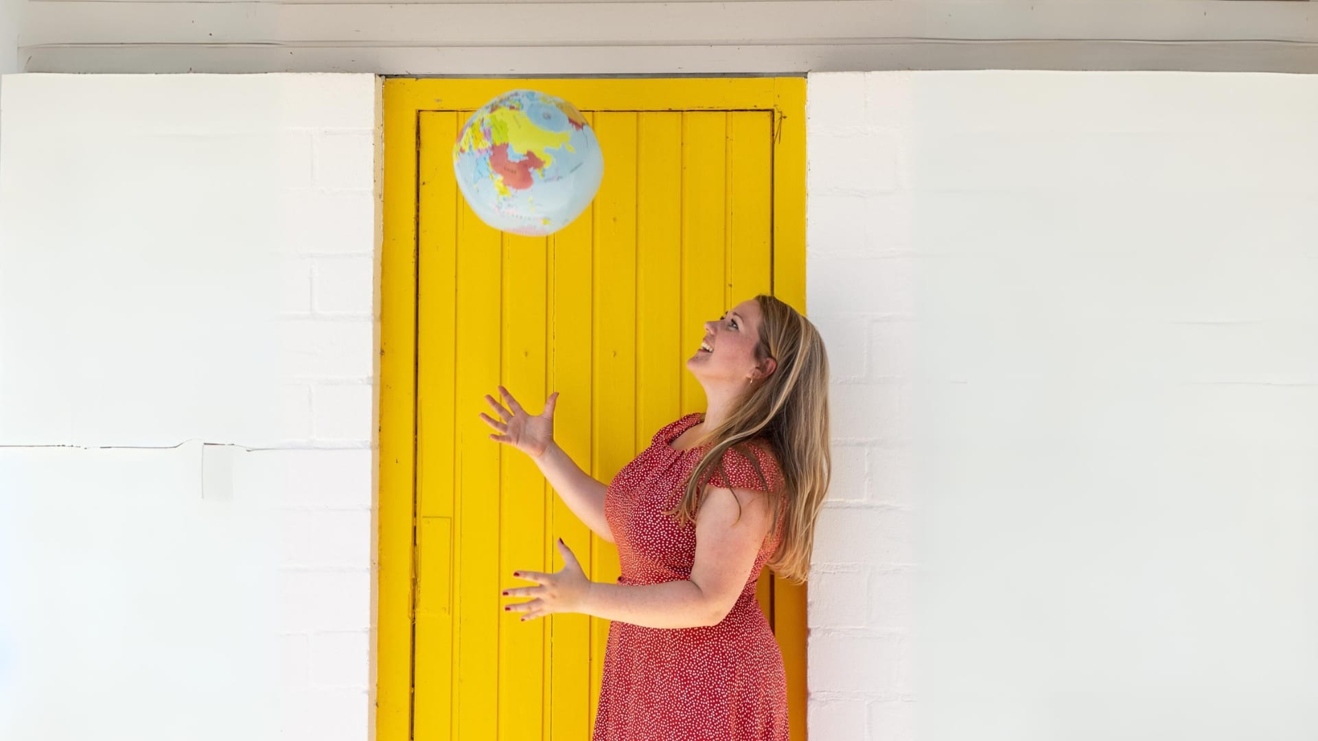 Frau wirft Globus vor gelber Tür hoch